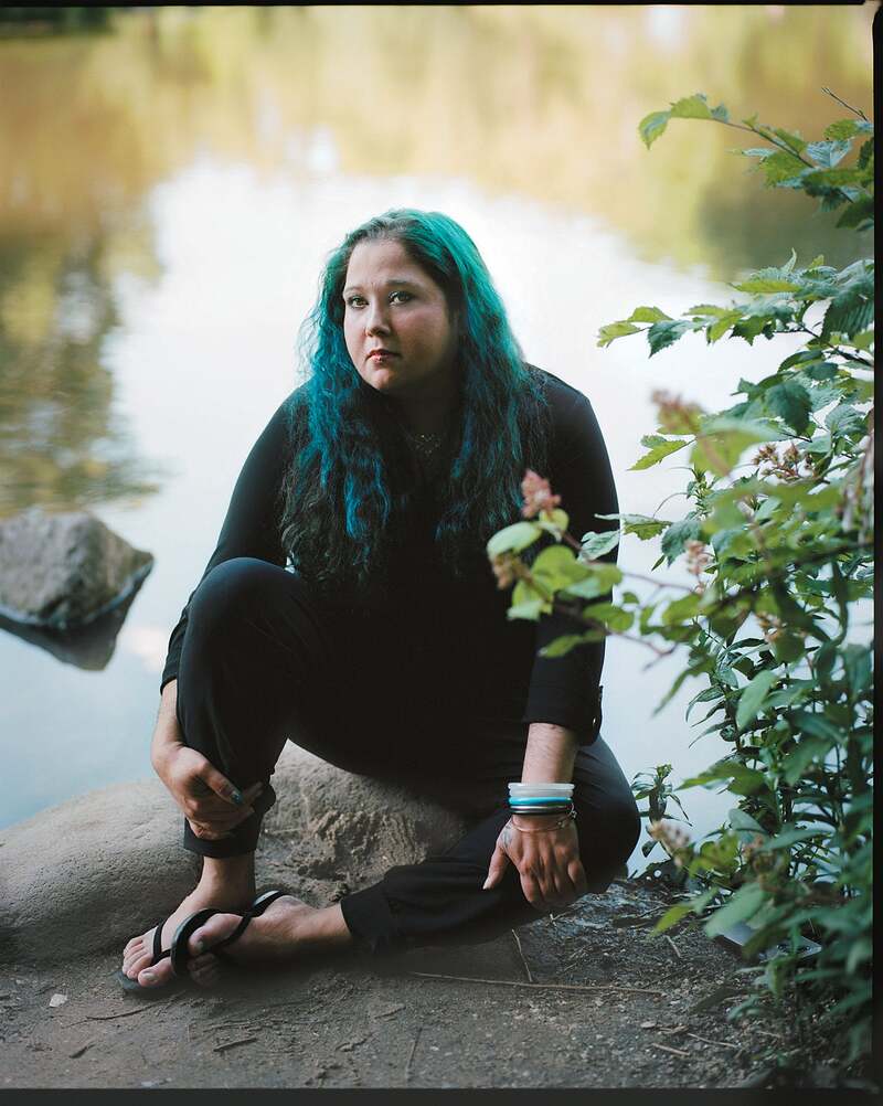 Maria Mazurkevich looking pensive, sitting on a tree branch by a pond.